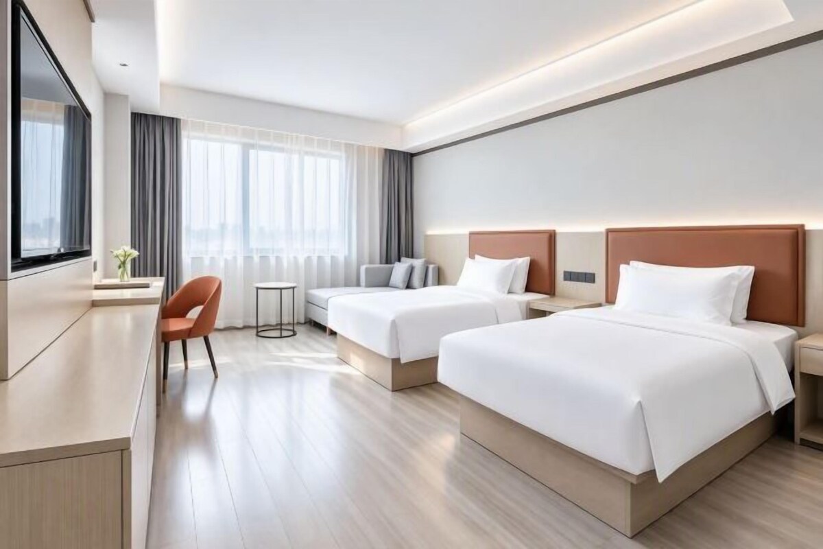 Hotellihuone, jossa on kaksi sänkyä, työpöytä, tuoli ja pieni pöytä.