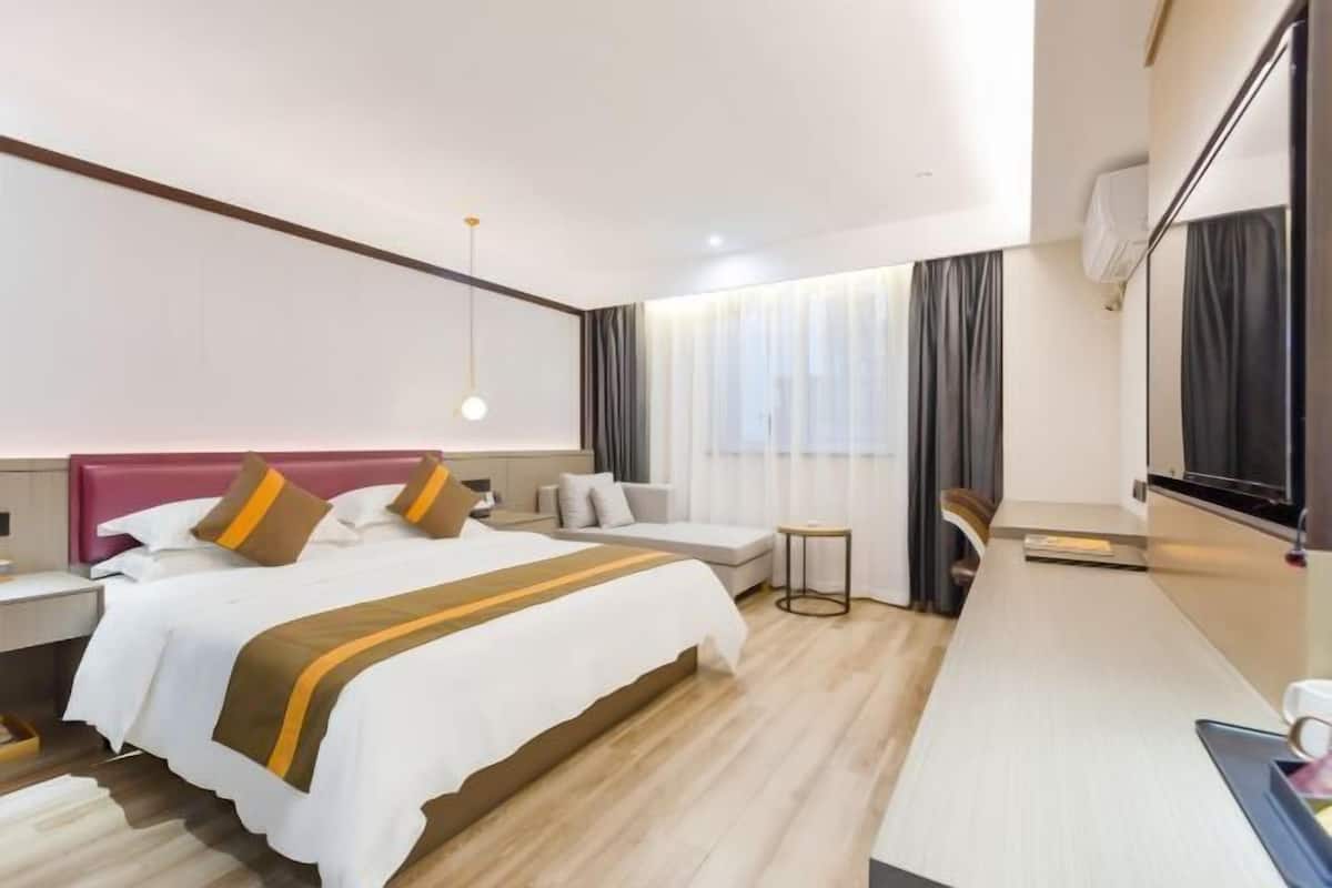 A hotel room with a bed, bedside tables, a small table, a sofa, a TV, and a window with curtains.