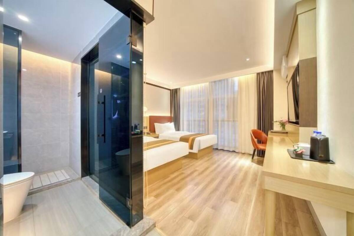 A hotel room with a glass partition, a bed, a desk, and a chair.