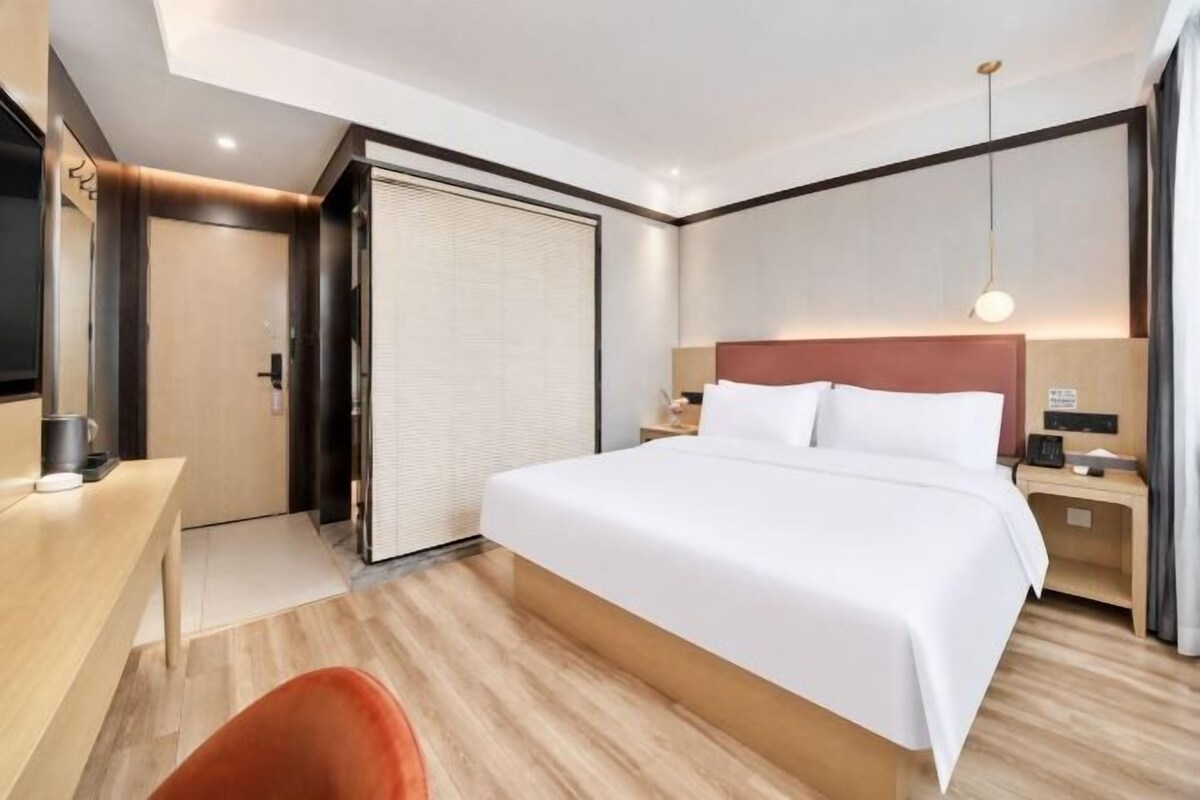 Hotellihuone, jossa on sänky, yöpöytä, lamppu ja työpöytä tuolilla.