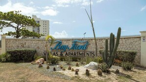 Une enseigne indiquant « Bay Front Villas & Apartments », avec un mur de pierres, des cactus et un arbre au premier plan.