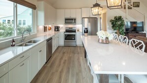 A modern kitchen with white cabinetry, stainless steel appliances, a large island with seating, and a view of the outdoors. - Gorgeous/Great Gulf Views! (Gulf Shores)