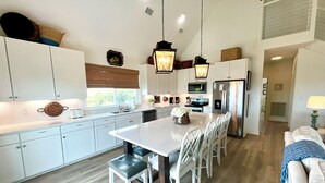 A modern kitchen with white cabinetry, a central island with seating, stainless steel appliances, and pendant lighting. - Gorgeous/Great Gulf Views! (Gulf Shores)