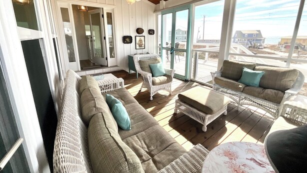 A spacious living room with a large window offering a view of the beach, a ceiling fan, and a wicker sofa with cushions. - Gorgeous/Great Gulf Views! (Gulf Shores)