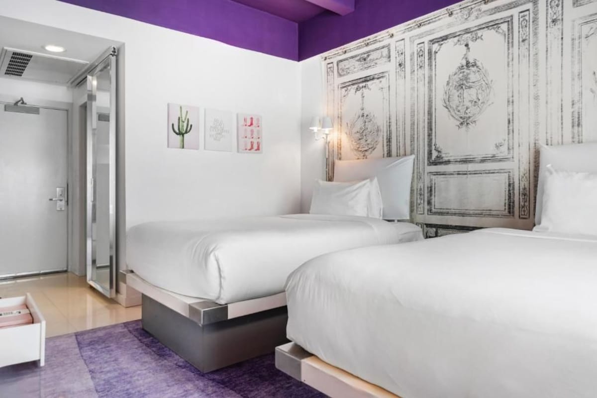 A bedroom with two beds, a purple rug, and a door leading to a bathroom.