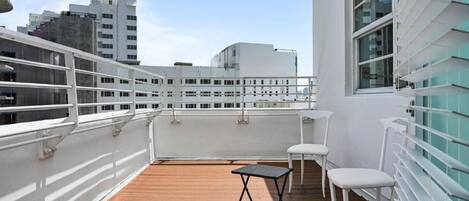 A rooftop terrace with a wooden deck, white railings, and a table with chairs.