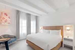 A modern hotel room with a large bed, a bedside table, a chair, and a window with curtains.