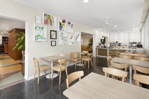 Um interior moderno com mesas, cadeiras, obras de arte nas paredes e uma área de cozinha.