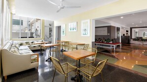 Un intérieur moderne comprenant un canapé, des tables, des chaises, un ventilateur de plafond et un escalier visible à travers un mur de verre.