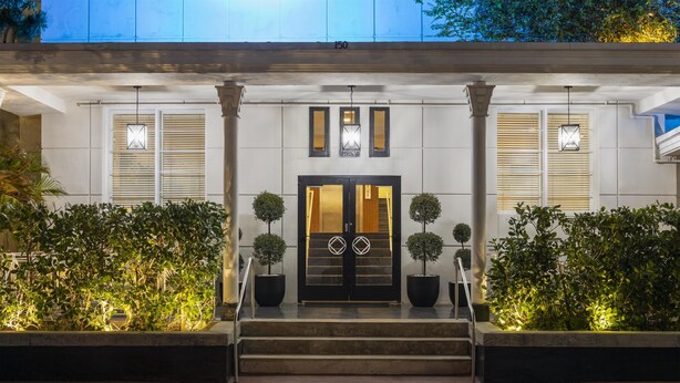 A hotel entrance with a double door, two potted plants, and a set of stairs leading up to the entrance.