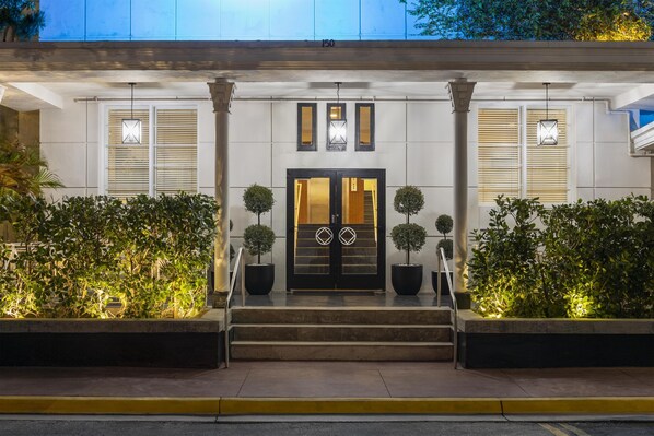 Entrada de hotel con puertas dobles, dos plantas en macetas y un conjunto de escalones que conducen a la entrada.