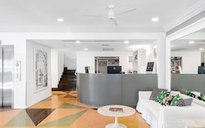 A hotel lobby with a reception desk, a staircase, a white sofa with patterned cushions, and a coffee table. - Townhouse Hotel (Miami Beach)