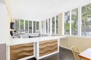 Una cocina moderna con encimera blanca, electrodomésticos integrados y ventanas amplias con persianas.