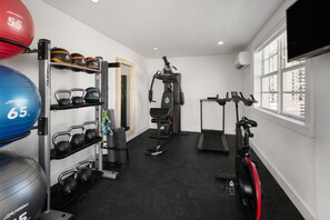 Uma academia doméstica com equipamentos de exercício, esteira e uma janela grande.