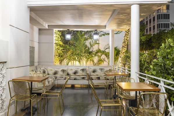 An outdoor seating area with tables and chairs, a sofa, and a view of greenery.