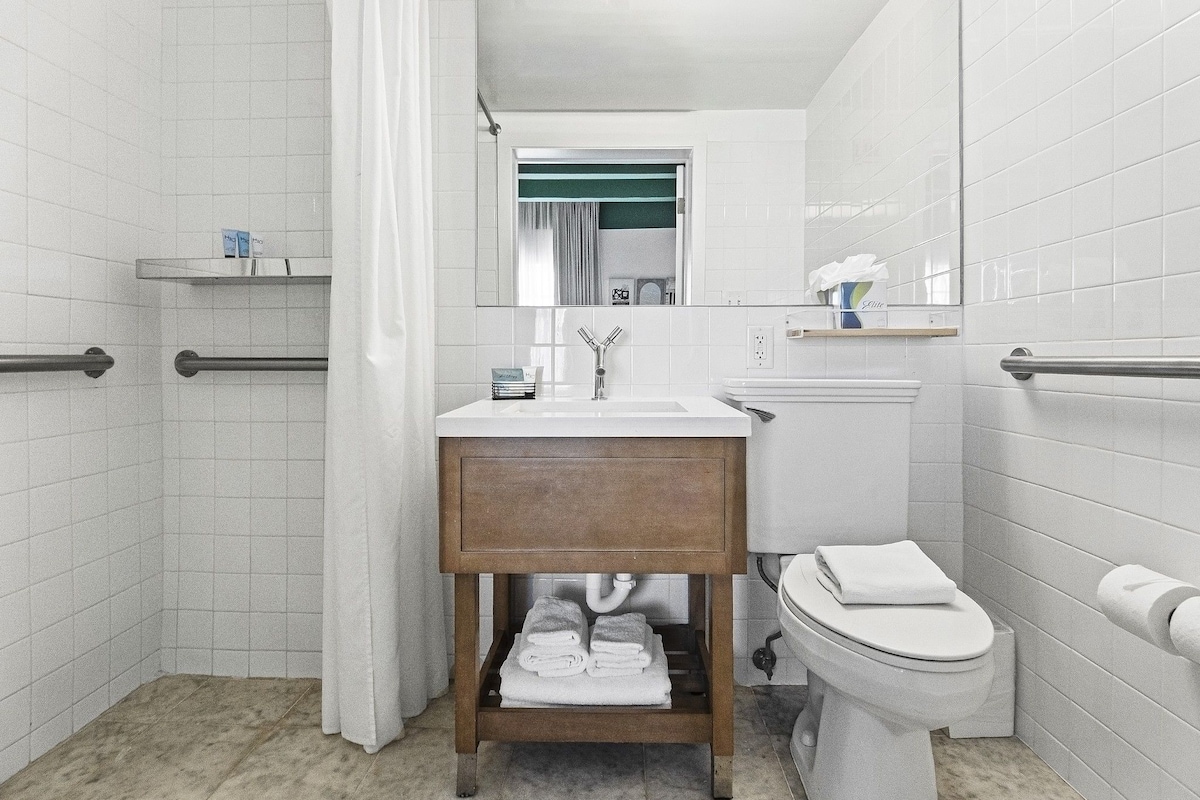 A modern bathroom with a white tiled wall, a wooden vanity, a sink, a toilet, and a shower area.