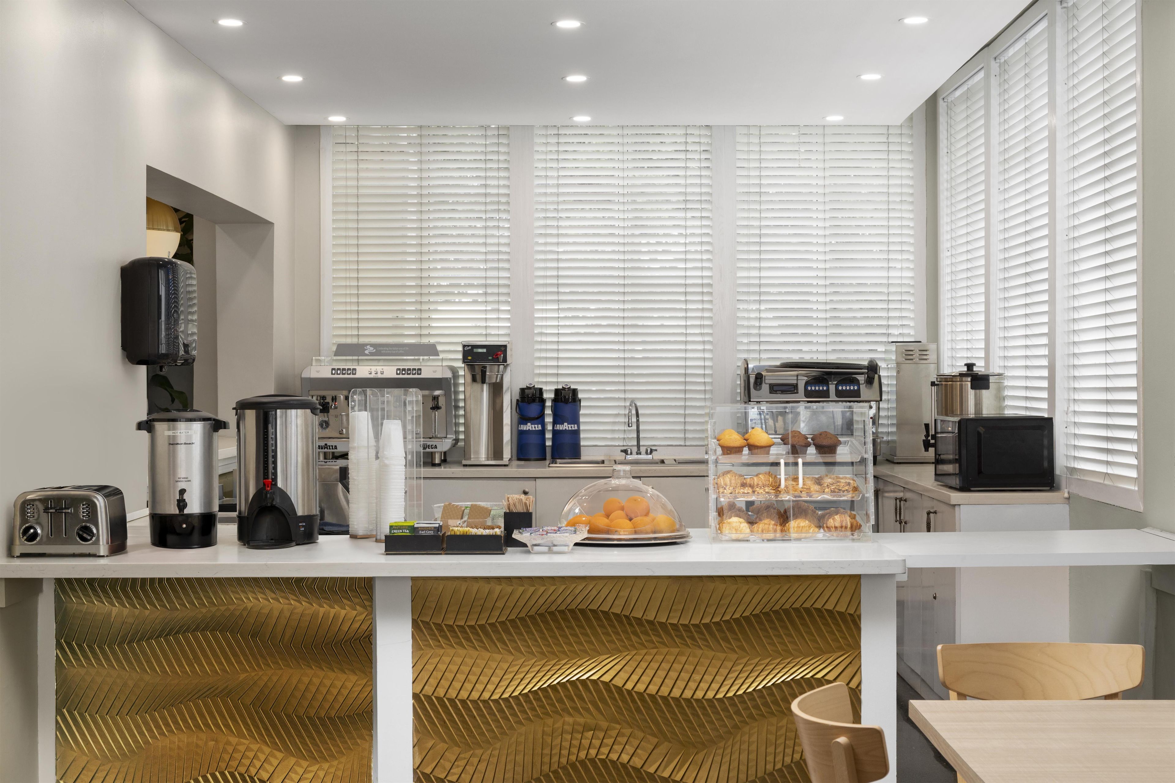 Uma cozinha moderna com bancada branca, máquinas de café, torradeira e uma vitrine com pão.