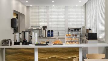 Uma cozinha moderna com bancada branca, máquinas de café, torradeira e uma vitrine com pão.