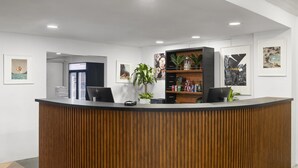 Un comptoir d’accueil avec un revêtement en bois, un écran HP noir, un vase blanc contenant une plante et des œuvres d’art encadrées accrochées aux murs.