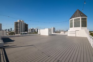 A rooftop terrace with a wooden deck, a small pavilion, and a city skyline in the background.