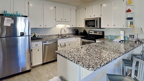 Una cocina moderna con armarios blancos, electrodomésticos de acero inoxidable, encimeras de granito y una isla central.