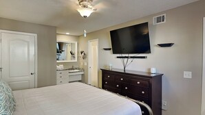 Un dormitorio con cama, cómoda, televisor y baño al fondo.