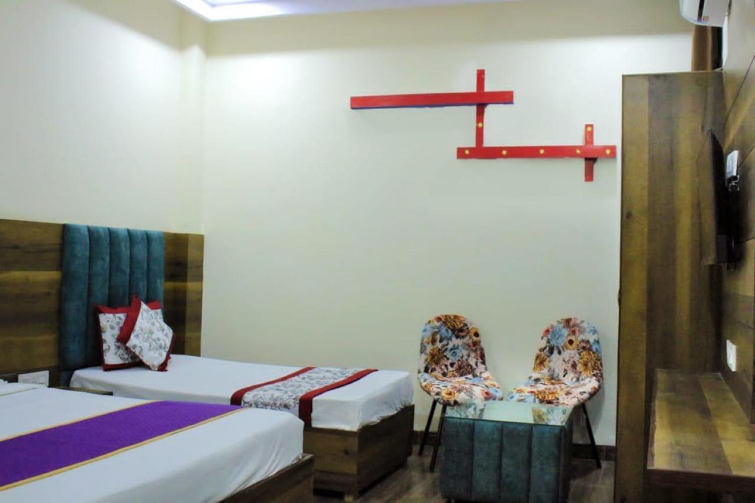 A hotel room with two beds, a small table, chairs, a wooden wardrobe, and a red cross decoration on the wall.