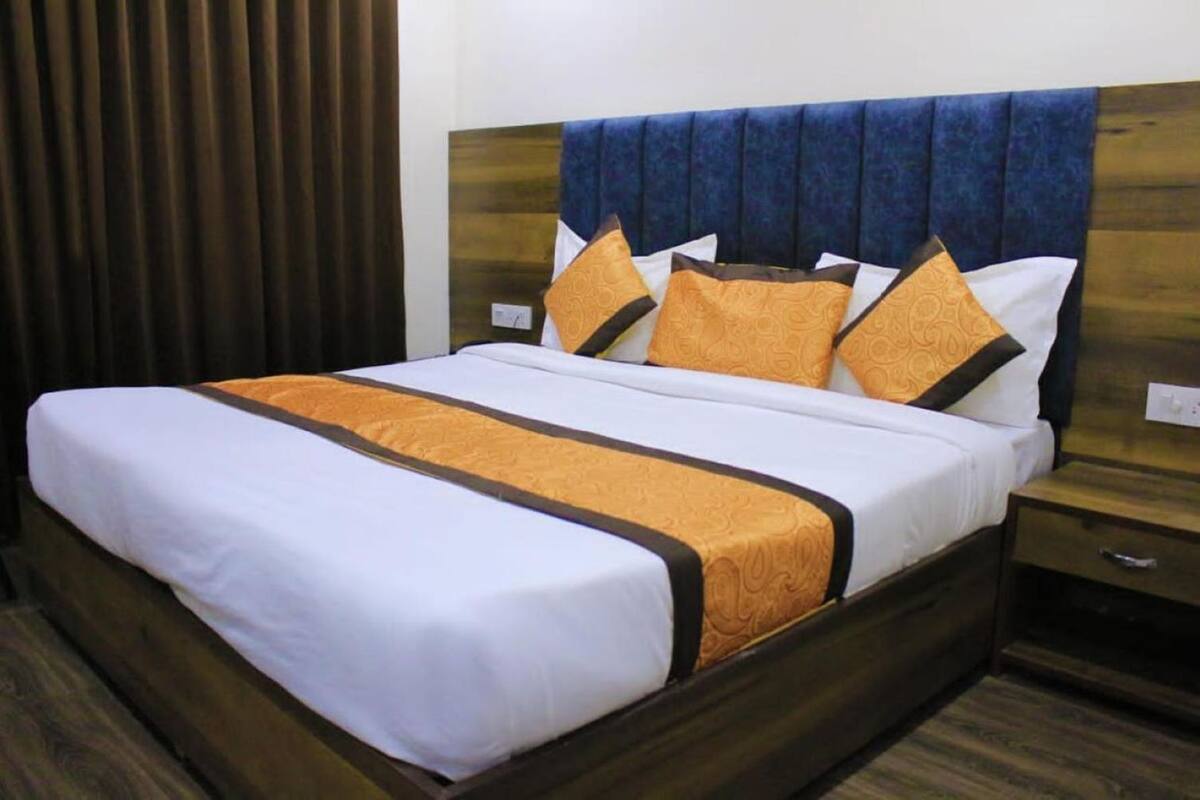 A neatly made bed with a white and orange bedspread, a wooden headboard, and a wooden nightstand with a drawer.