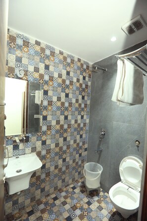 A bathroom with a tiled floor, a sink, a toilet, and a shower area. - HOTEL KANDA CONTINENTAL  (Amritsar)