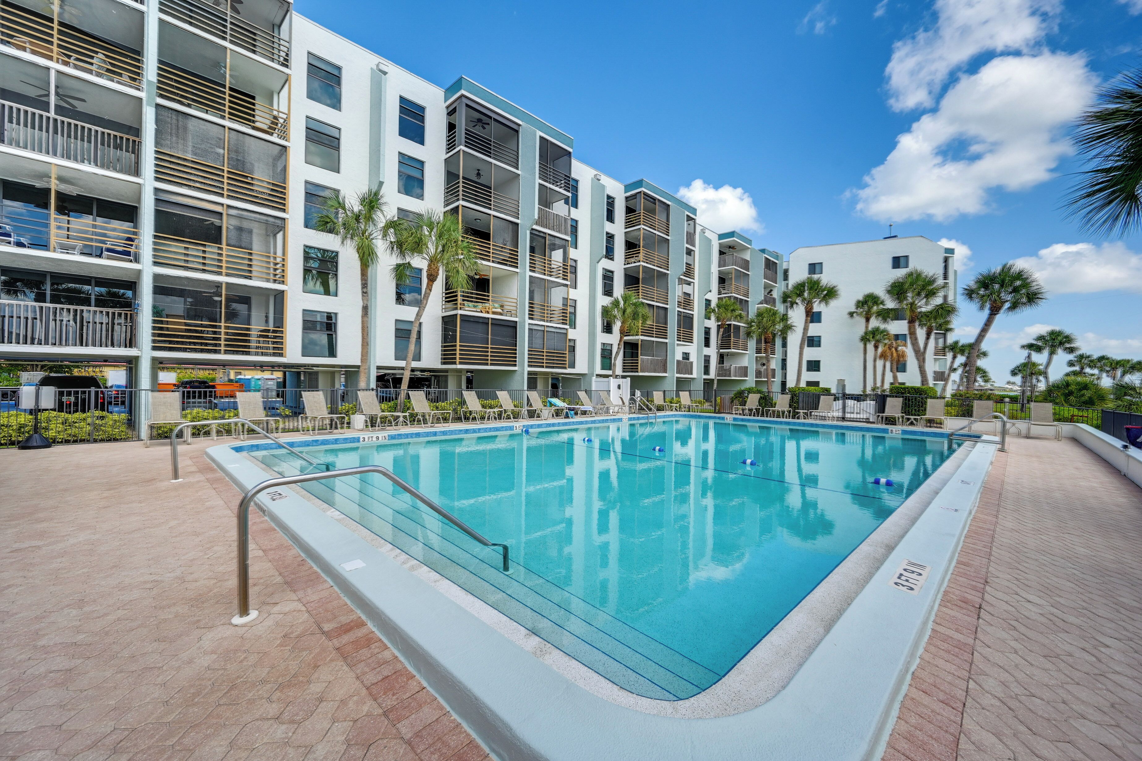 A modern hotel with a swimming pool, multiple balconies, and palm trees.