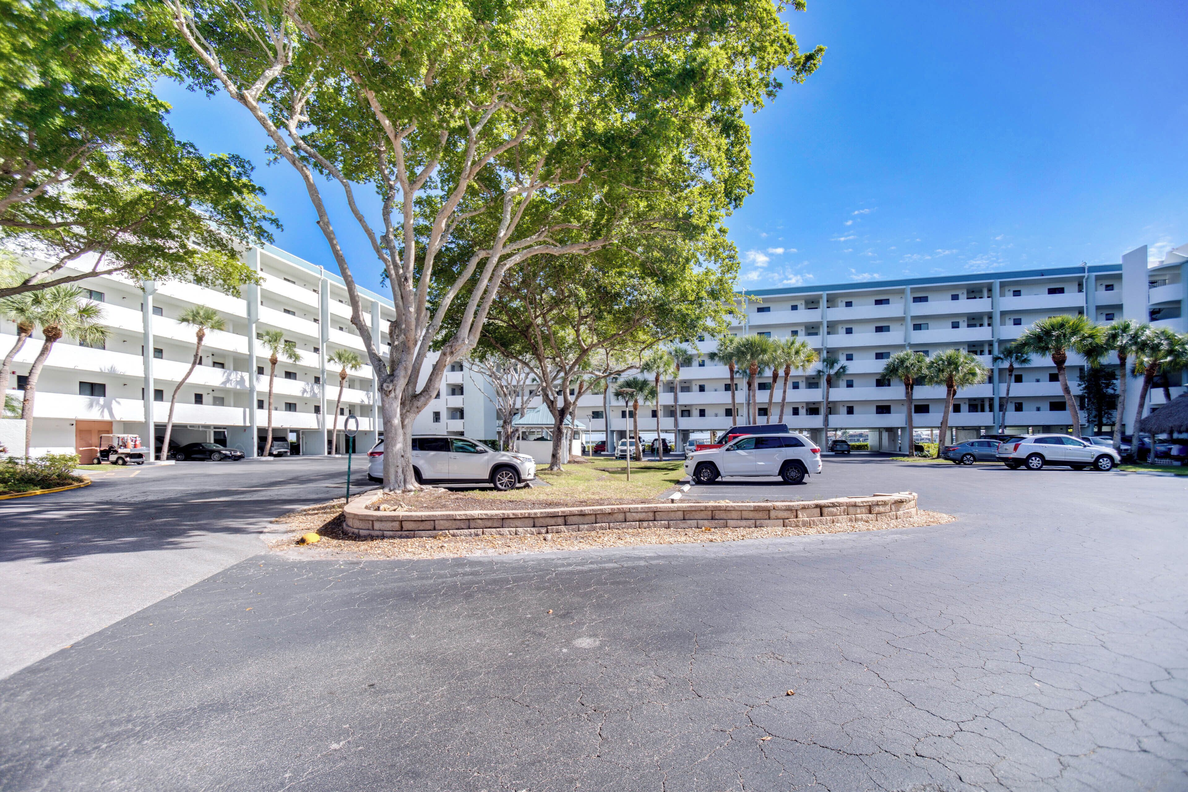 A multi-story hotel with a parking lot, palm trees, and a clear blue sky.