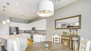 A modern kitchen with white cabinetry, a central island, stainless steel appliances, and a dining area with a wooden table and chairs. - Hot Tub & On-site Hiking: Phoenix Retreat! (Phoenix)