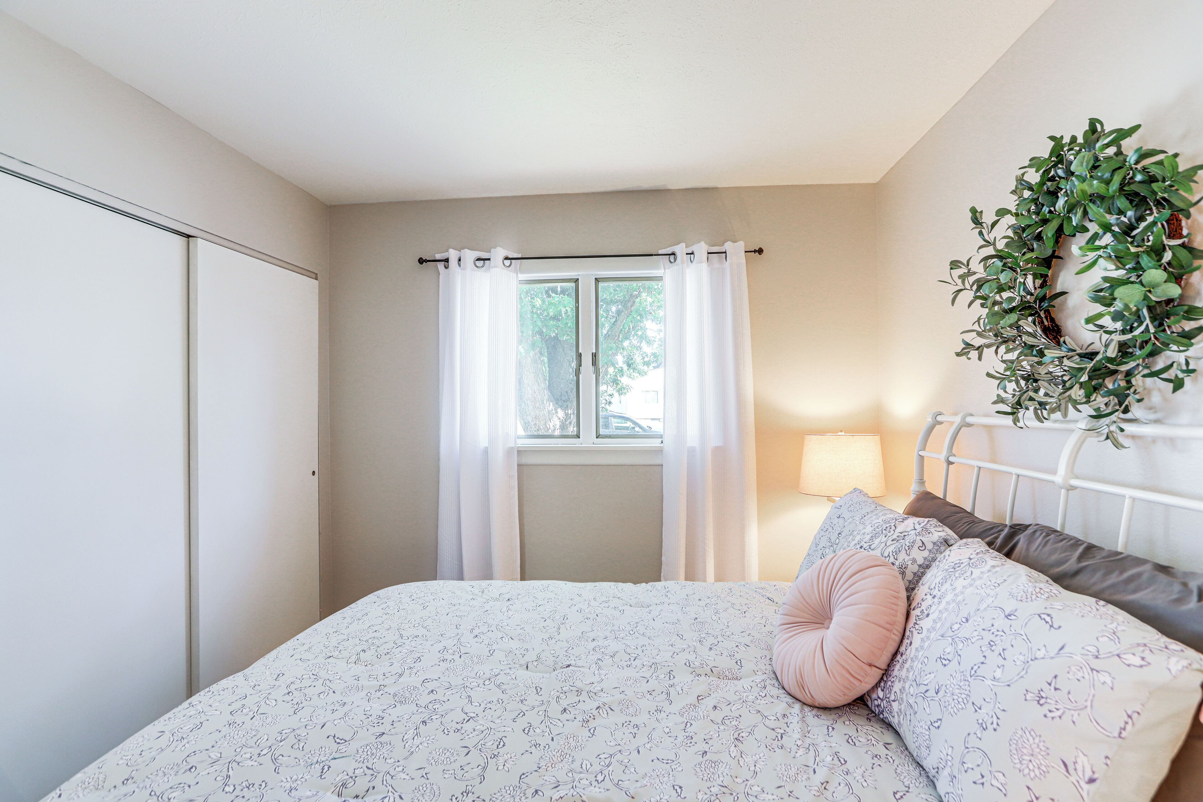 A bedroom with a bed, a window with curtains, a bedside lamp, and a wall-mounted plant.
