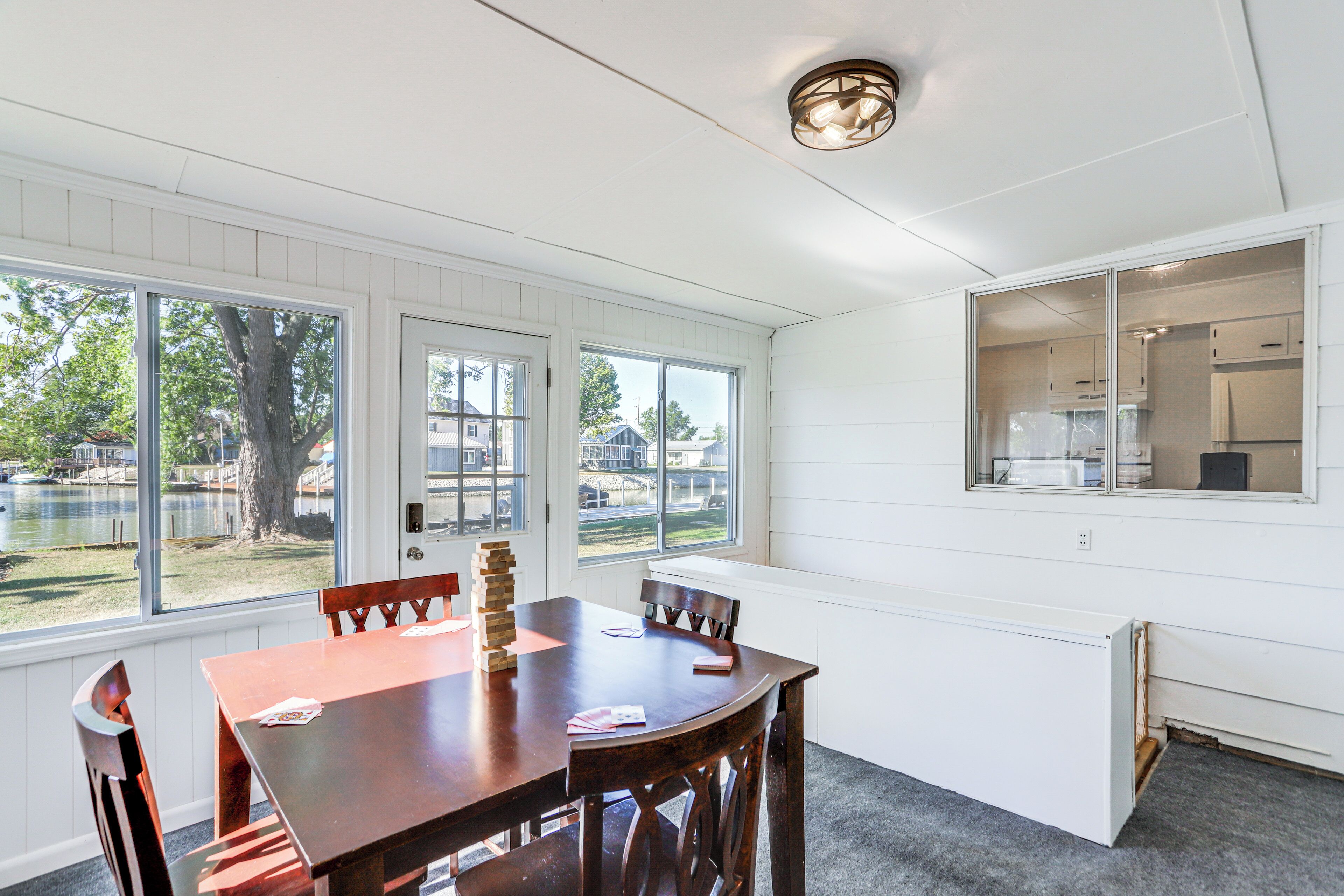 A dining area with a wooden table and chairs, large windows, and a view of a backyard.