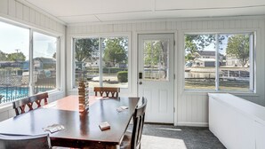 Una habitación con una mesa de madera, sillas y vistas a una piscina a través de amplios ventanales.