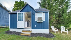 Un piccolo capanno blu con la porta aperta, che mostra un angolo cottura all'interno. Due sedie Adirondack bianche sono posizionate all'esterno.