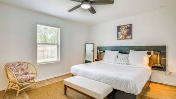 Un dormitorio con cama, banca, silla, ventilador de techo, ventana y lámpara de pared.