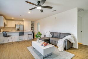Una sala de estar moderna con un sofá gris, una mesa de centro blanca con libros y un ventilador de techo.