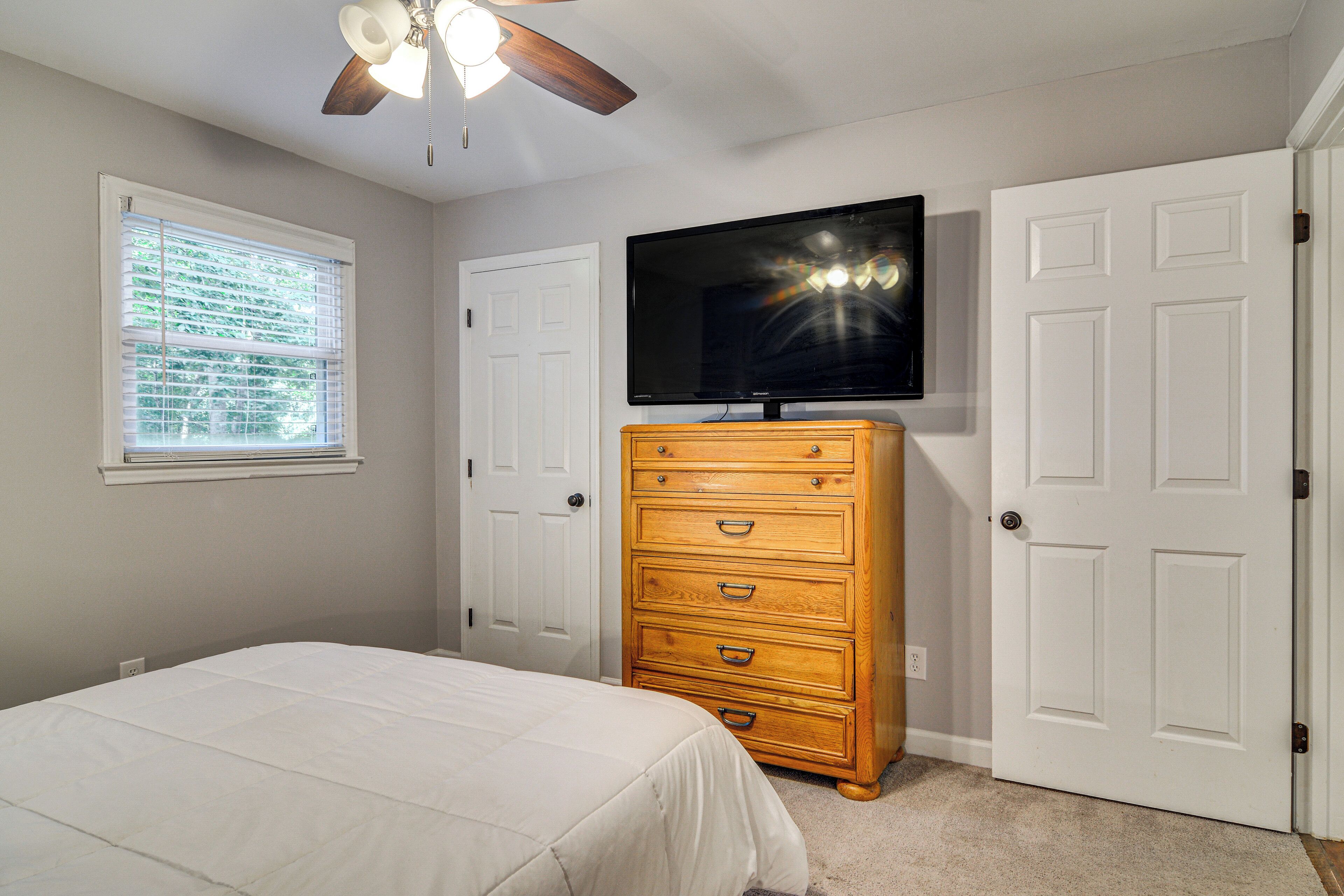 A bedroom with a bed, a dresser, a ceiling fan, a TV, and two doors.