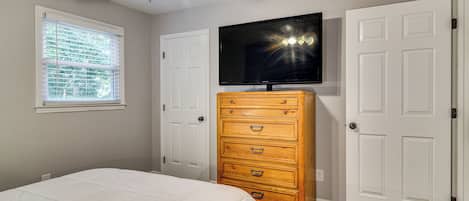 A bedroom with a bed, a dresser, a ceiling fan, a TV, and two doors.