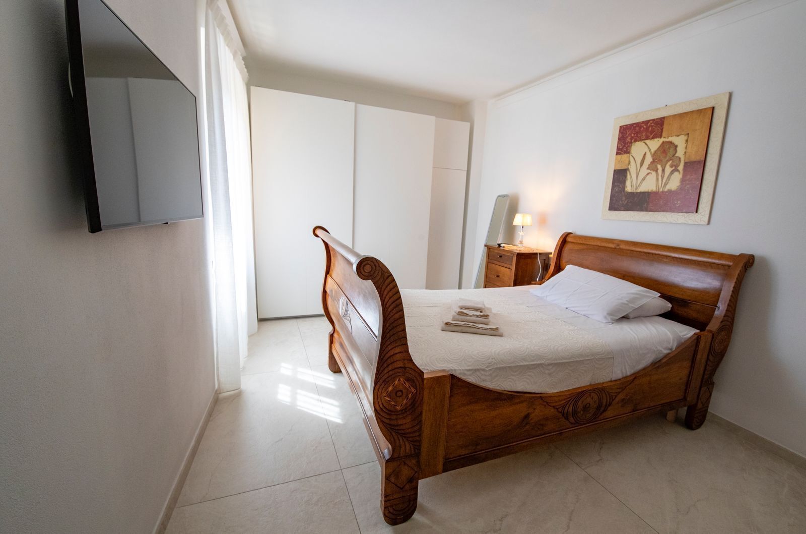 A neatly arranged bedroom with a wooden bed, a bedside table with a lamp, and a framed picture on the wall.
