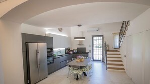 Una cocina moderna con horno empotrado, refrigerador y pileta. Hay una mesa de comedor con sillas y una escalera que lleva a otro nivel.