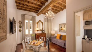 A cozy living room with a wooden ceiling, a dining area with a table and chairs, a sofa with cushions, and a kitchen area with cabinets and appliances. - The Inn at the Spanish Steps Exclusive Collection - Roberto Di Rienzo (Rome)