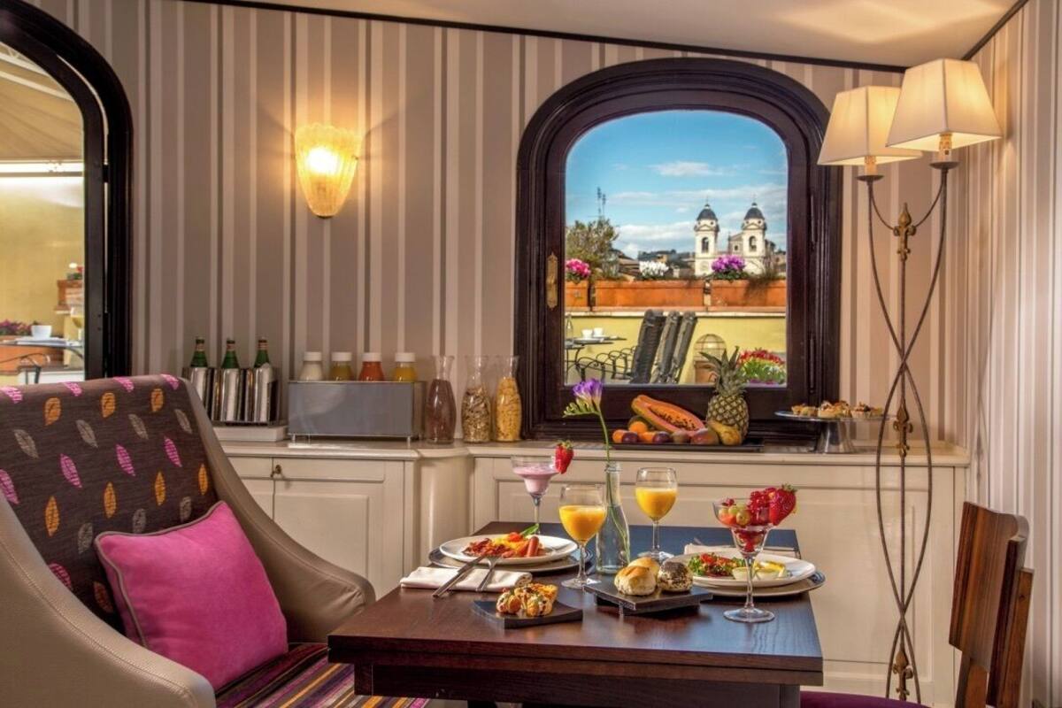 Un comedor con una mesa lista para el desayuno, vista a una iglesia y papel tapiz a rayas.