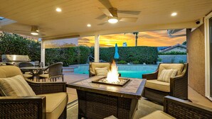An outdoor patio with a fire feature, seating, and a view of a swimming pool at sunset.