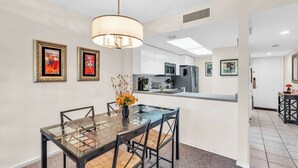 A modern dining area with a glass table and chairs, a pendant light, and artwork on the walls. - H-247 - Second Floor With Lake and Fountain View (Naples)