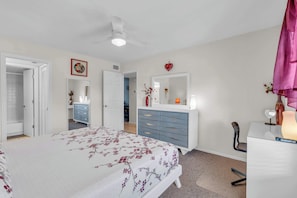 A bedroom with a bed, dresser, vanity, and a ceiling fan.