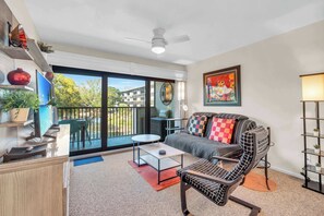 A modern living room with a sofa, coffee table, and a chair. There is a balcony with a table and chairs, and a painting on the wall. - H-247 - Second Floor With Lake and Fountain View (Naples)