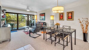 A modern living room with a dining table, chairs, and a sofa. There is a balcony with a view of the outside. - H-247 - Second Floor With Lake and Fountain View (Naples)