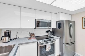 Une cuisine moderne avec des armoires blanches, un réfrigérateur en acier inoxydable, un four à micro-ondes encastré, une plaque de cuisson et une machine à café.
